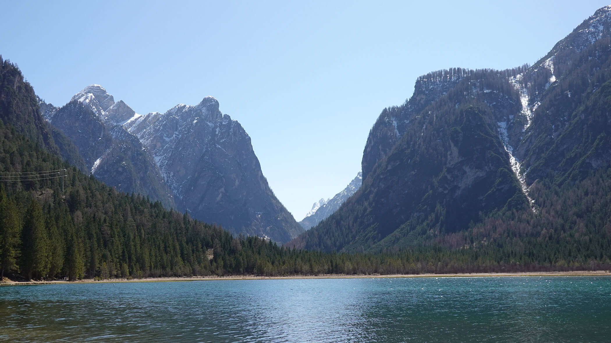 Ein klarer, blauer See mit Kiefern und hohen, schneebedeckten Bergen unter einem hellen, klaren Himmel. - Garni Tschurtschenthaler