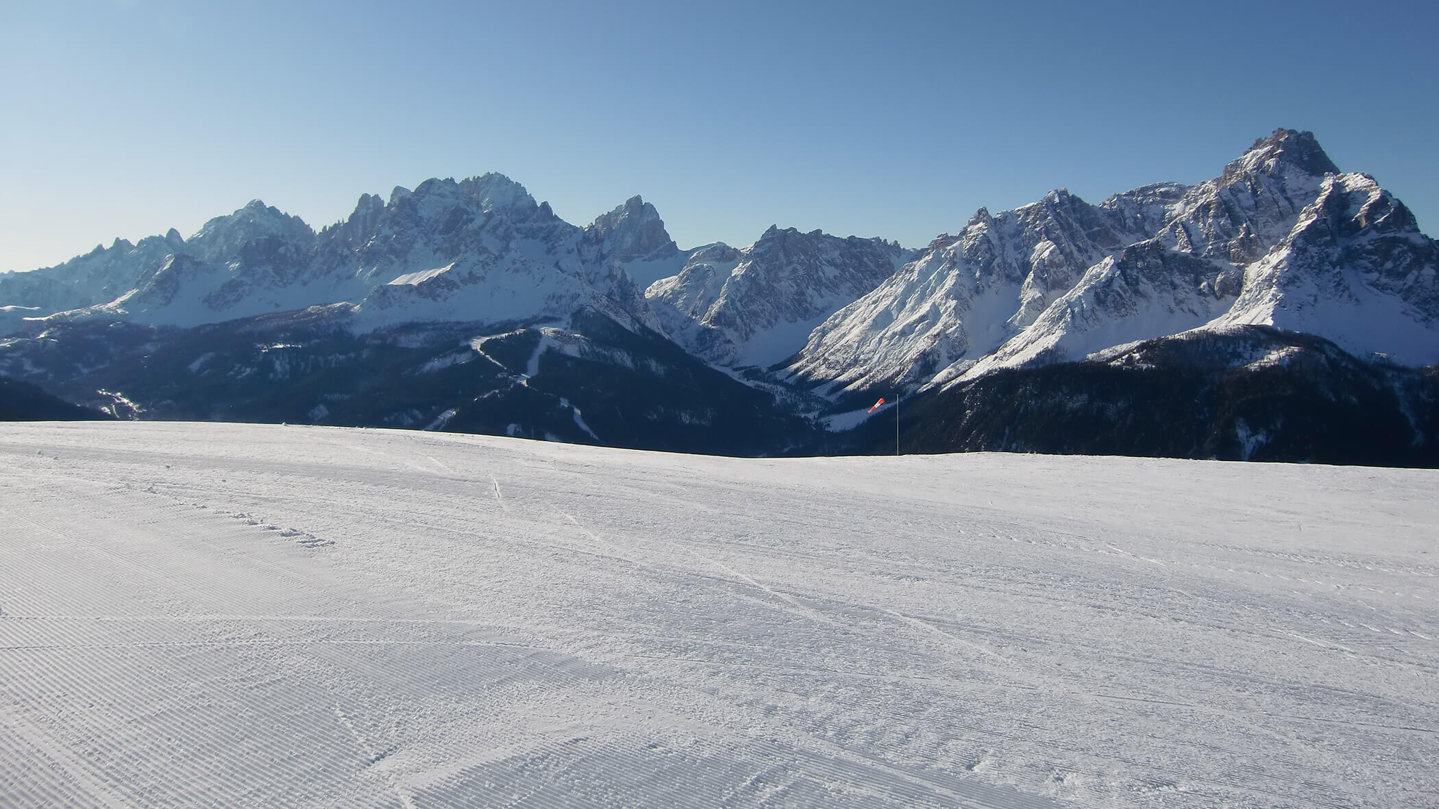 Verschneite Skipiste mit entferntem Gebirge und blauem Himmel im Hintergrund. - Garni Tschurtschenthaler